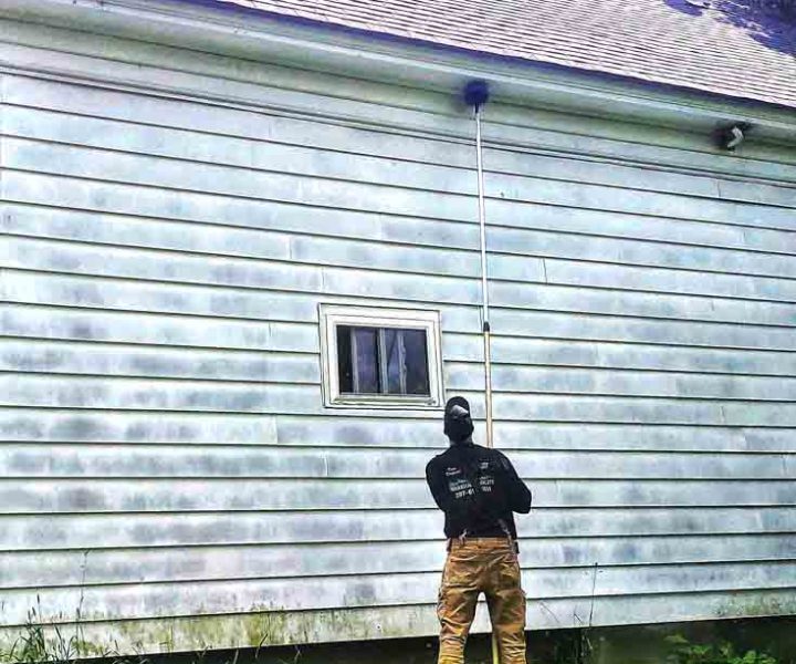 Wildlife Chief technician using an extension pole to clear pests from the eaves of a Skowhegan home